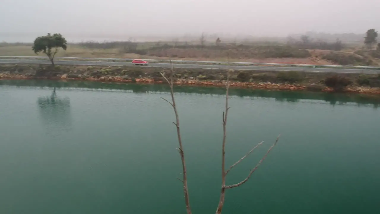 A car passing through two lakes in a foggy morning