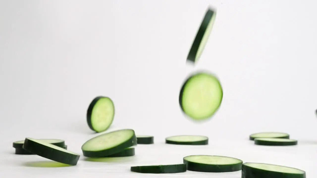 Bright green fresh cucumber slices falling flipping and bouncing on white backdrop in slow motion