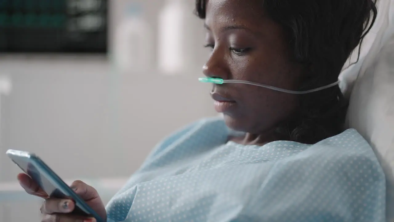 Black woman Patient in Hospital with Saline Solution Volumetric Infusion Pump using mobile phone on examination couch African women lying in hospital bed with smart mobile phone while in hospital