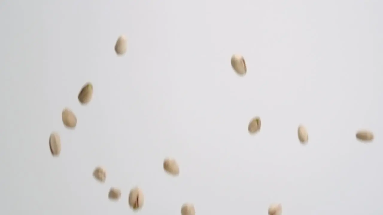 Whole pistachio nuts in shells raising down on white backdrop in slow motion