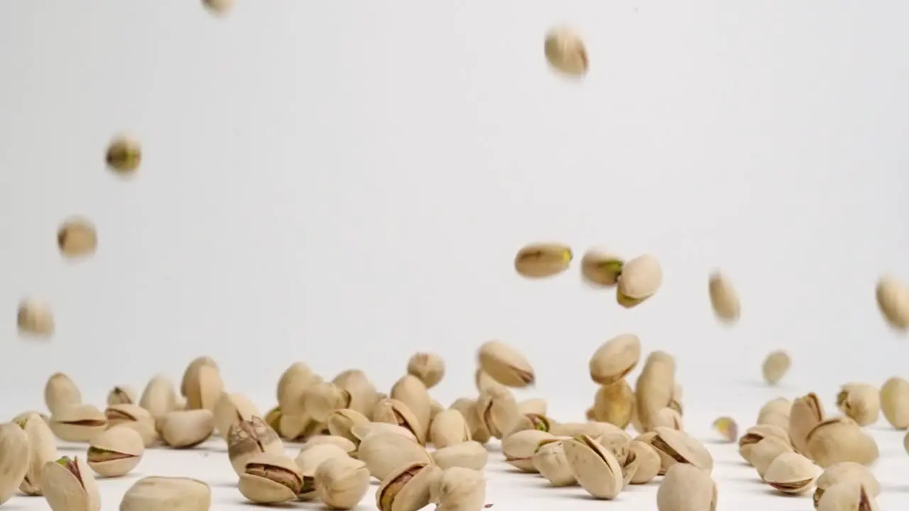 Whole pistachio nuts in shells falling onto white table top and bouncing around in slow motion