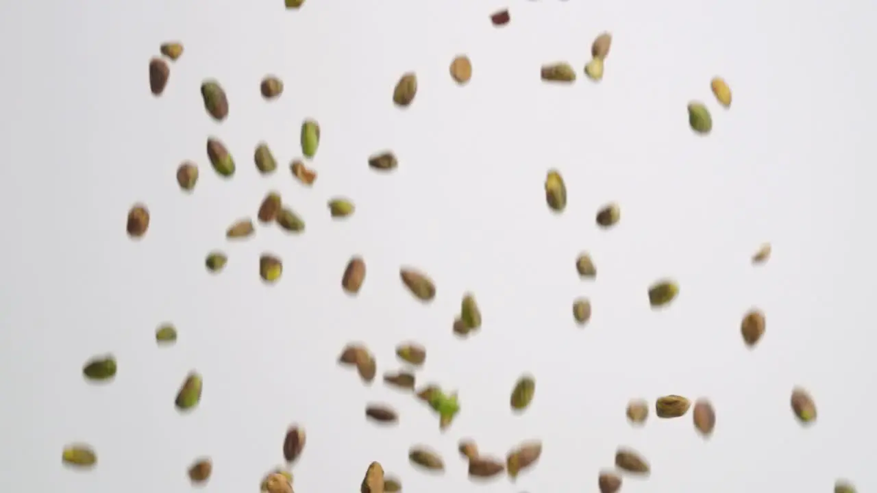 Shelled pistachio nuts raining down on white backdrop in slow motion