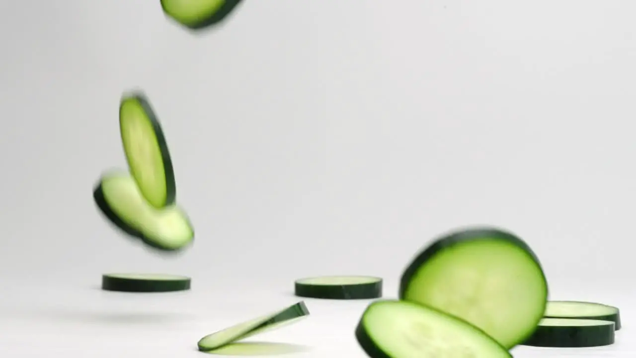 Fresh green cucumber coins falling onto table bouncing flipping and settling into a pile in slow motion