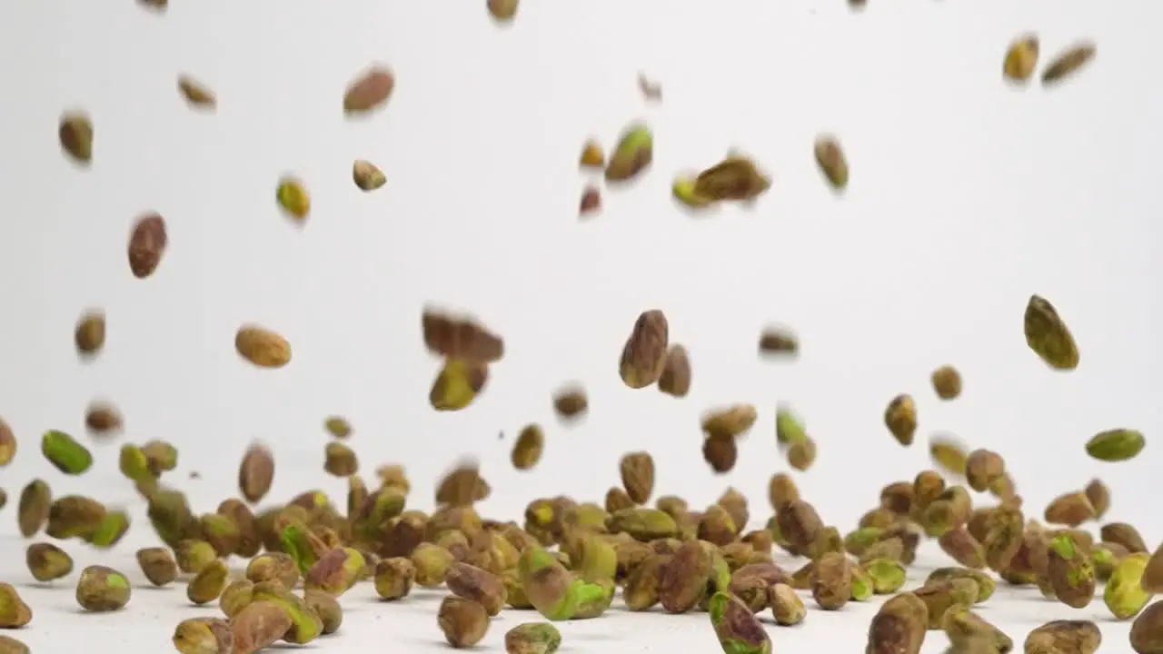 Shelled pistachio nuts raining down on white table top and bouncing into a pile in slow motion