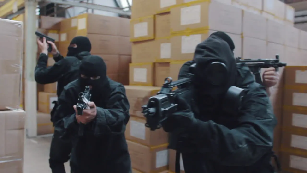 A special forces military team raid a warehouse with guns drawn wearing balaclavas an gas masks