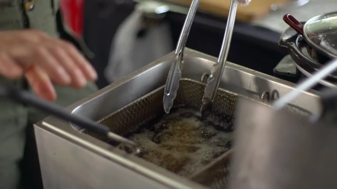 Meat balls stirred with tongs while inside vat of boiling hot oil filmed as close up shot in handheld slow motion style