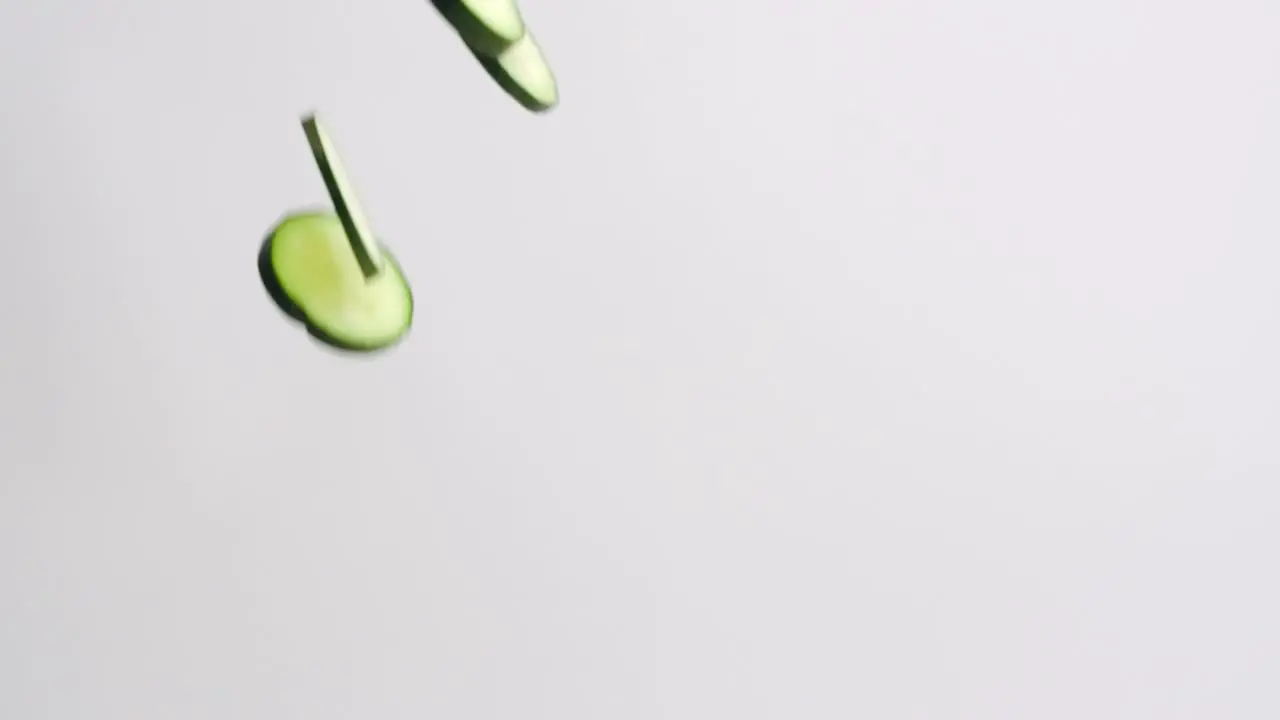 Fresh bright green cucumber slices raining down on white backdrop in slow motion