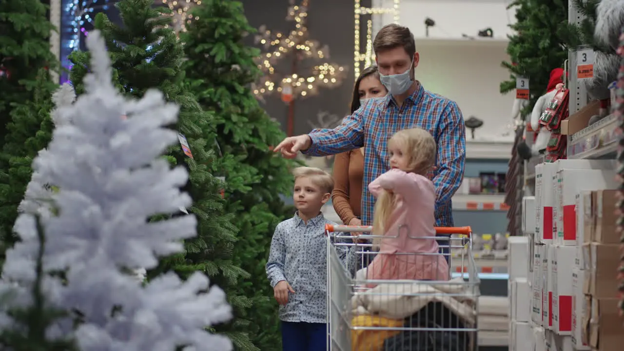 The family chooses a Christmas tree in the store together A happy family in medical masks in the store buys Christmas decorations and gifts in slow motion