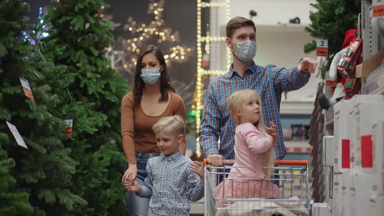 A family of four people mother father and children choose together a Christmas tree A happy family in medical masks in the store buys Christmas decorations and gifts in slow motion