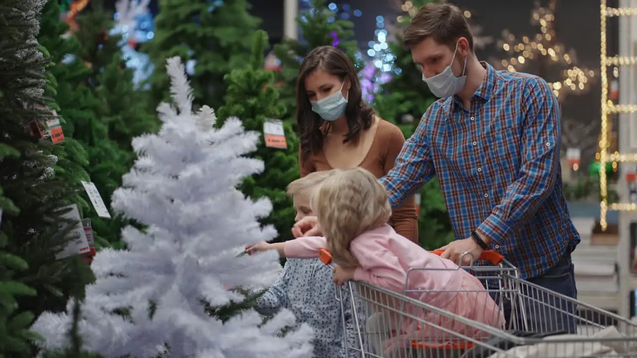 Mom Dad's daughter and son get out together christmas tree A happy family in medical masks in the store buys Christmas decorations and gifts in slow motion