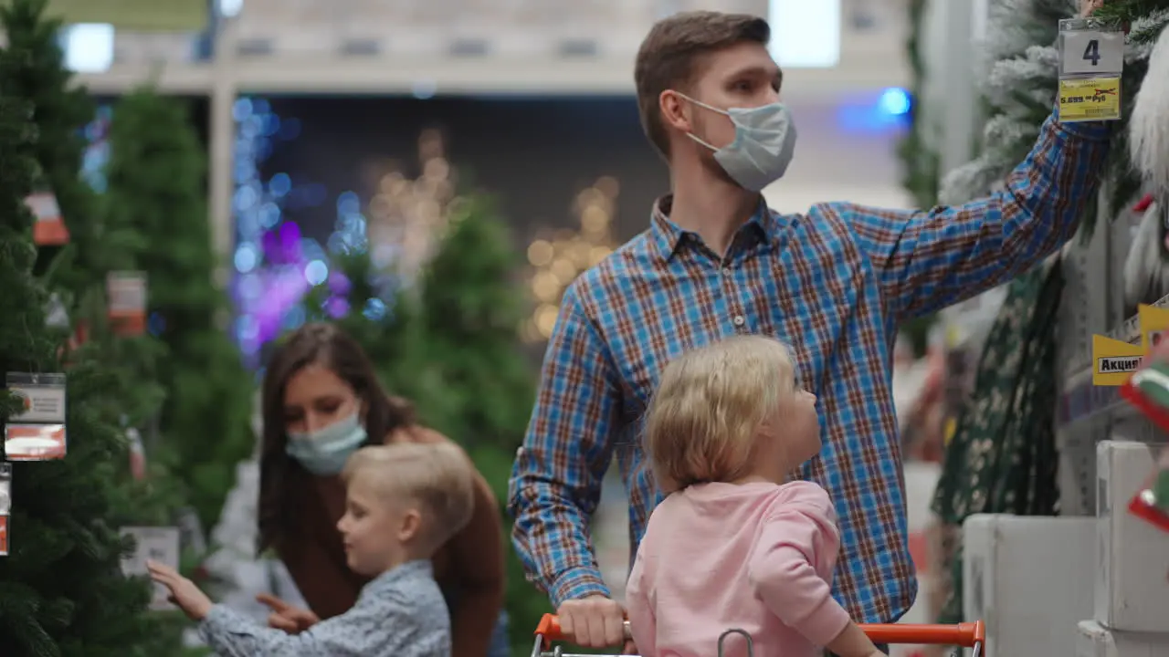 A father and mother with two children son and daughter are choosing Christmas Tree toys and home decorations on Christmas Eve during the pandemic and quarantine family in medical masks in the store