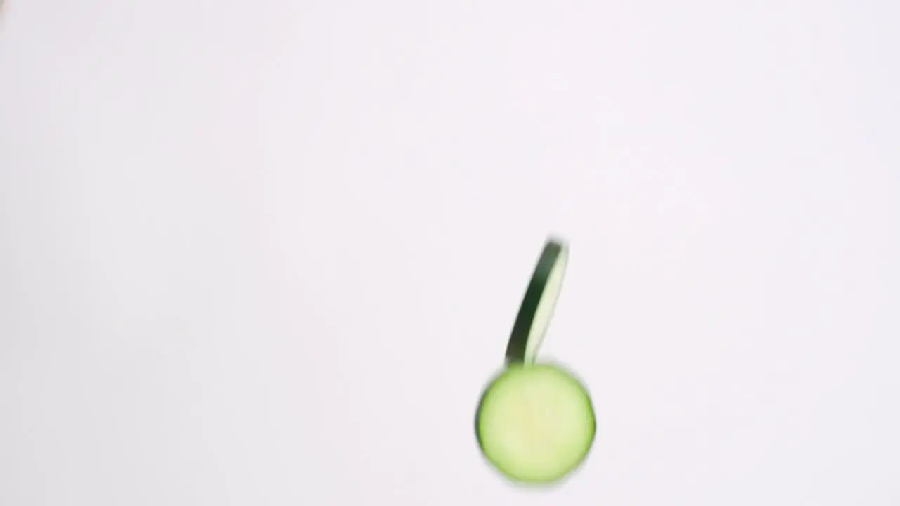 Slow motion cucumber slices raining down on white backdrop