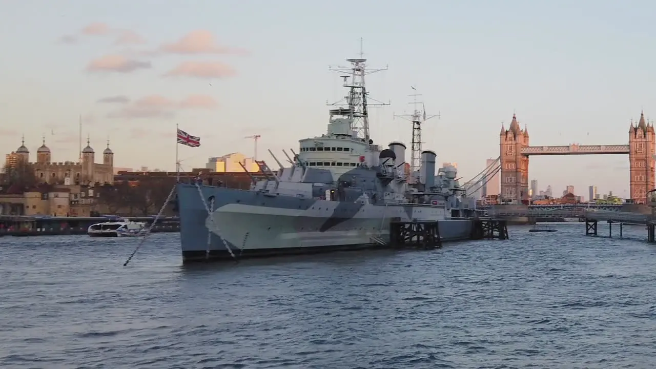 View of a military ship in front of London tower and bridge at sunset over Thames river