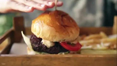 Tasty burger with french fries on a wooden tray Female hands touching it to start taking Slow Motion shot