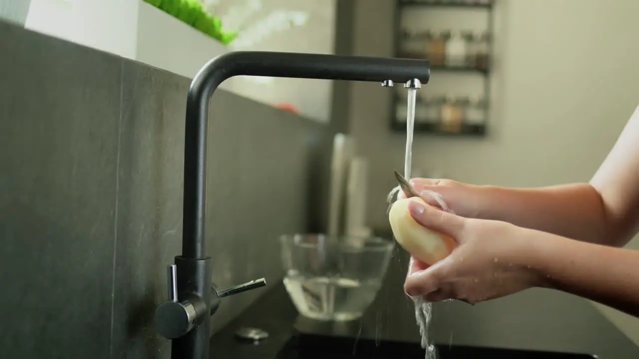 Women's hands under running water from a tap peel potatoes