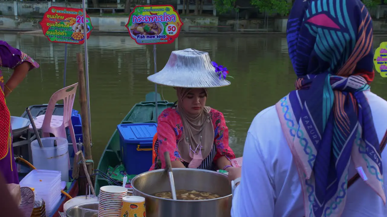 Thai woman with traditional hat selling asian food in the banks of Klong Hae floating market river