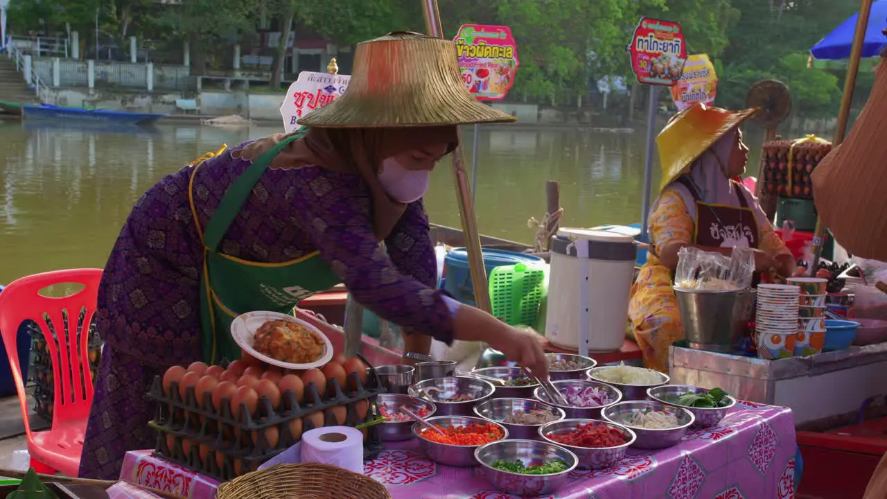 Young Thai woman wearing a mask and typical cap preparing her vegetables to sell at a local street stall