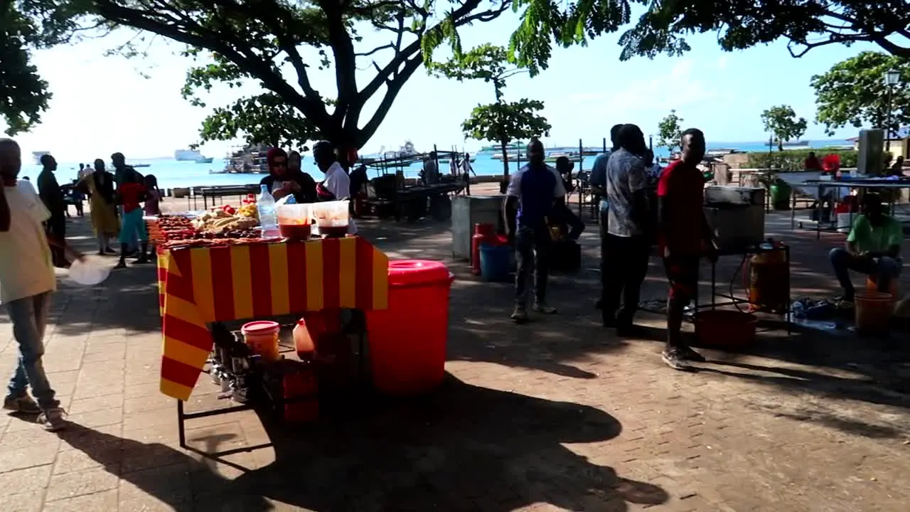 Local tanzanian people at food stalls in park approaching tourists to sell typical food