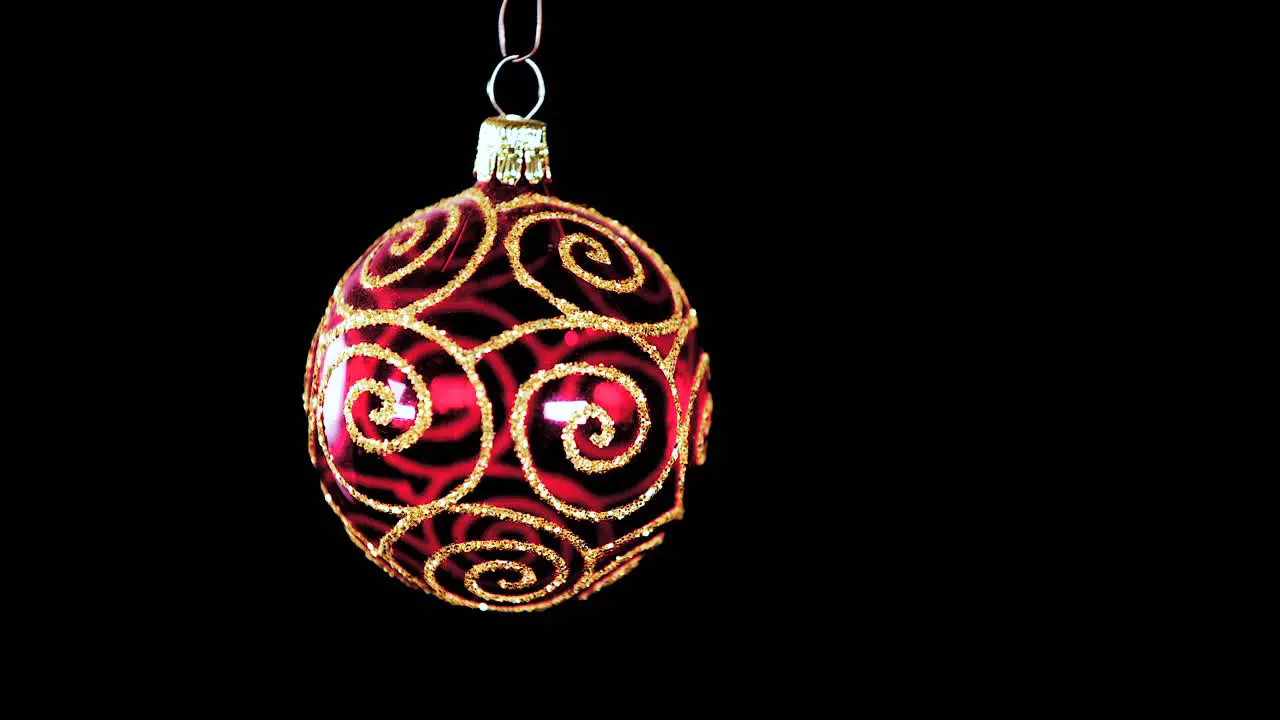 single red clear Christmas ball ornament with golden glitter stripes and black background close up