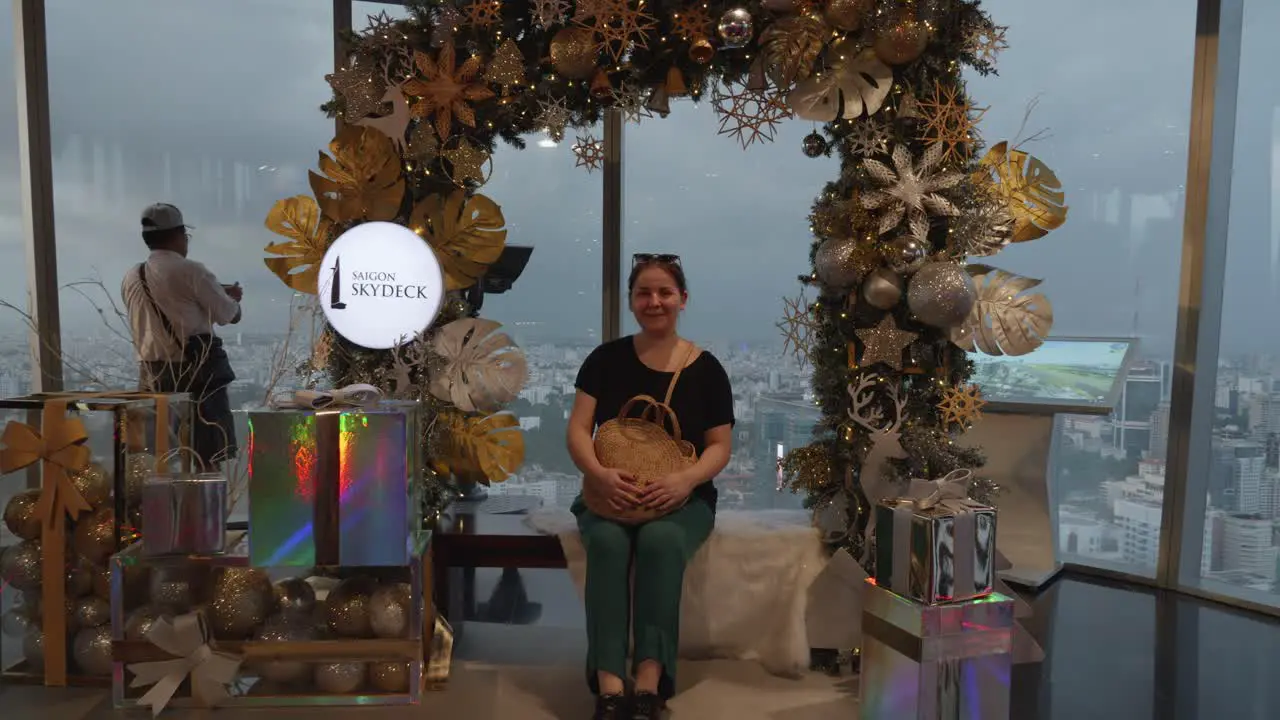 A woman in her thirties sits on a bench surrounded by a festive Christmas display at the Skydeck of the Bitexco Financial Tower in Ho Chi Minh Vietnam