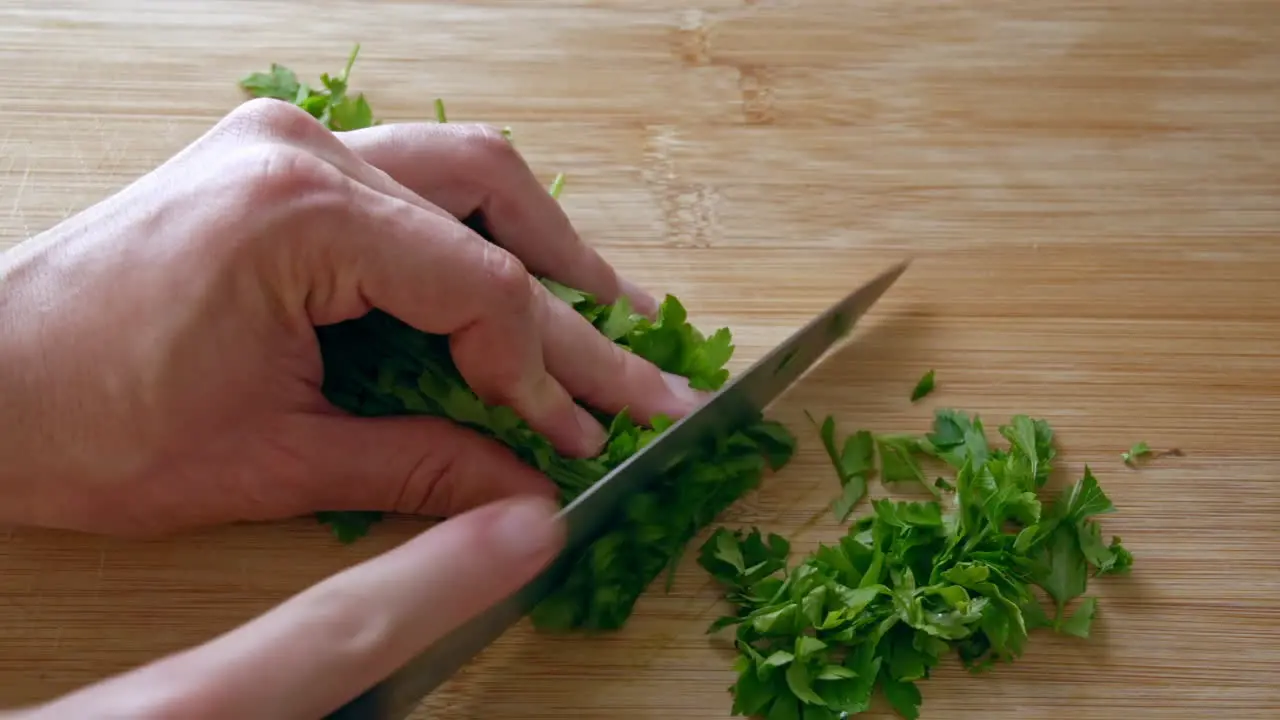 A close up of chopping parsley with a knife on a wooden board