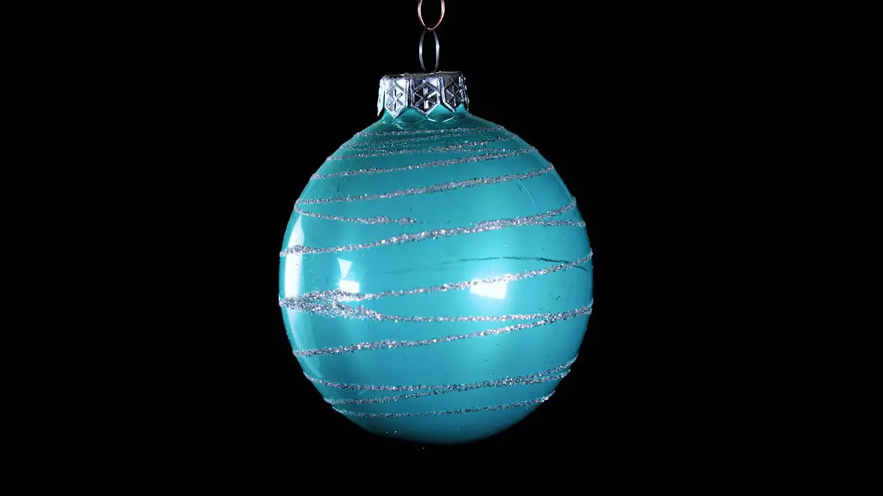 single blue turquoise Christmas ball ornament with glitter stripes and black background close up