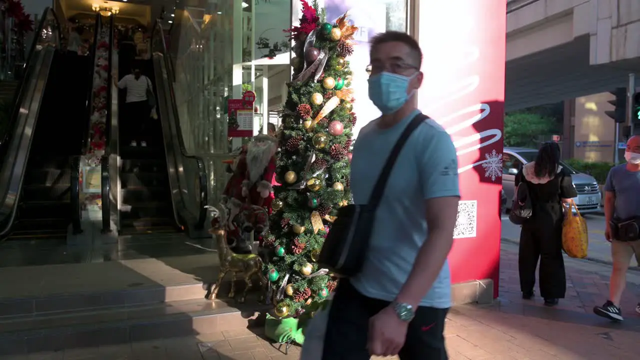 Pedestrians wearing face masks walk past a flower and home deco products shop with a Christmas tree and ornaments displayed at its entrance in Hong Kong