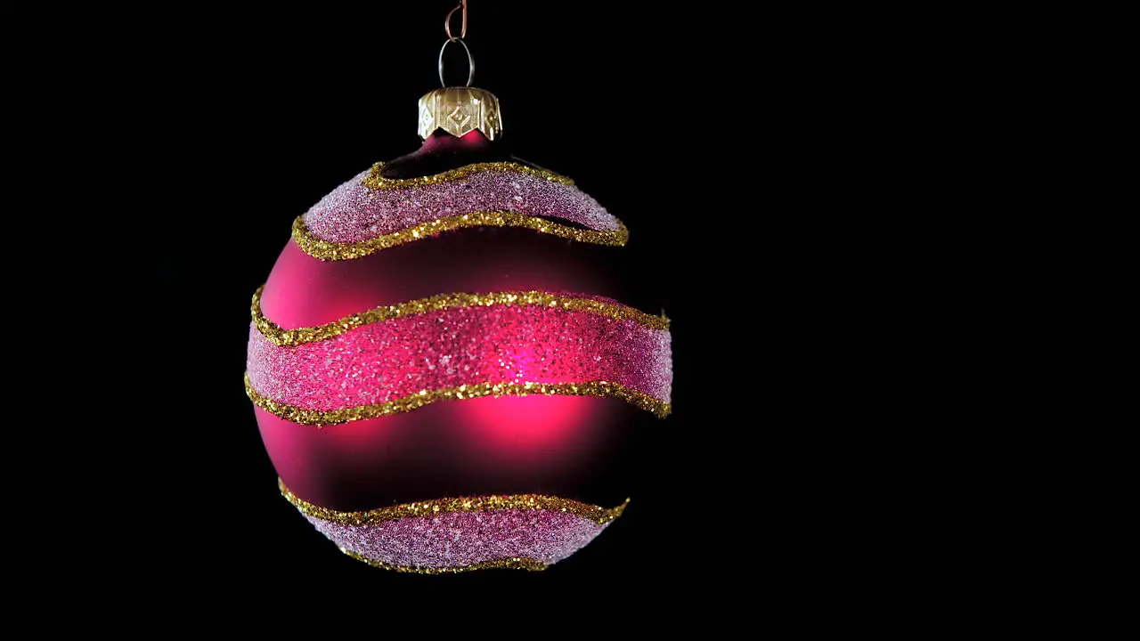 single red Christmas ball ornament with golden silver glitter stripes and black background close up