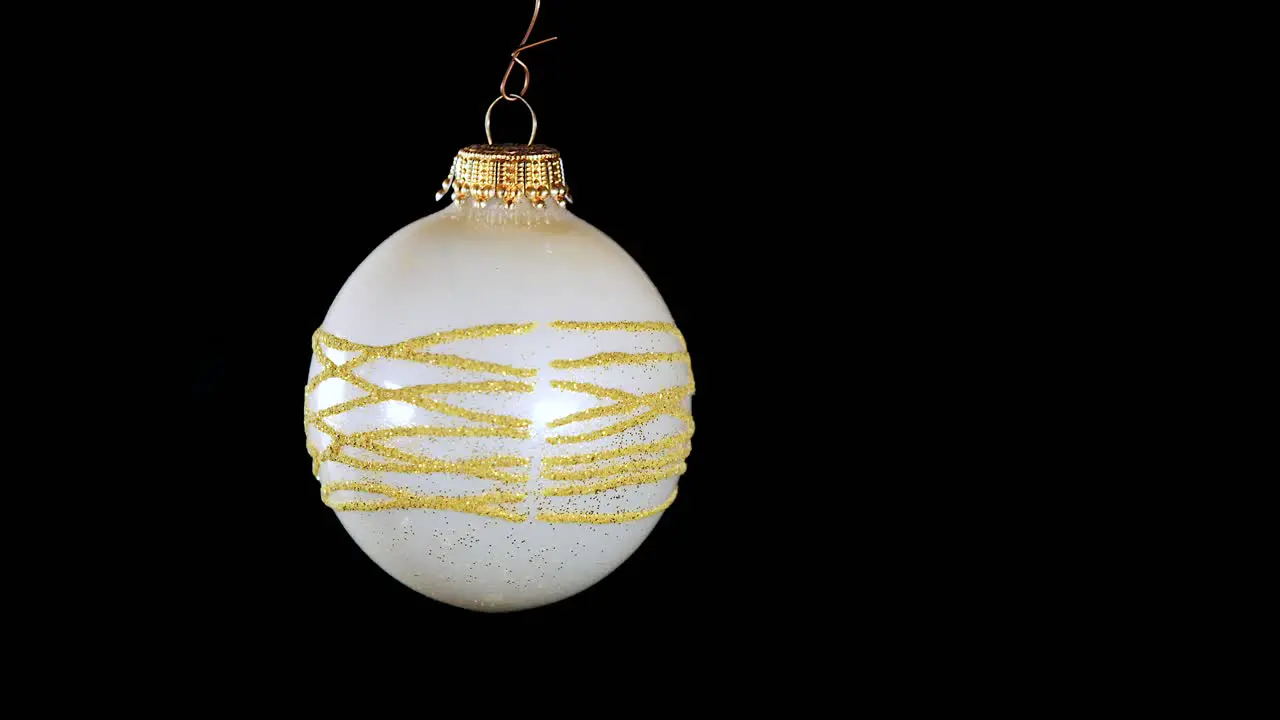 single white Christmas ball ornament with golden glitter stripes and black background close up