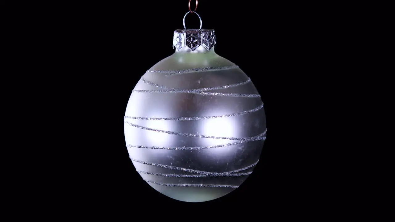 single silver Christmas ball ornament with glitter stripes and black background close up