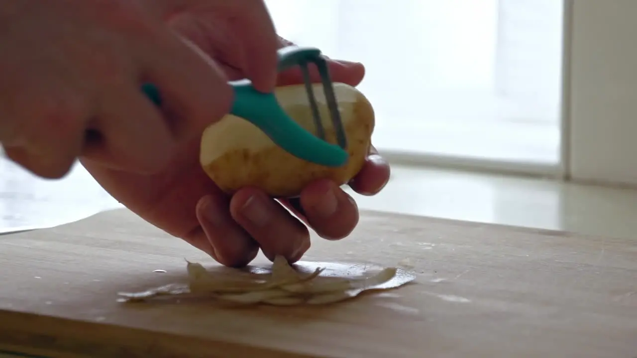 A close up of peeling a potato with a peeler