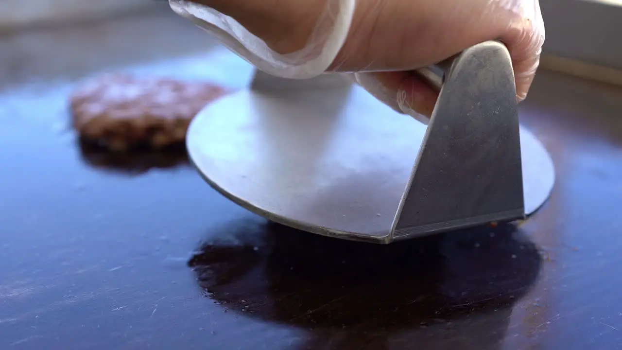 chef is pressing on piece of meat on grill