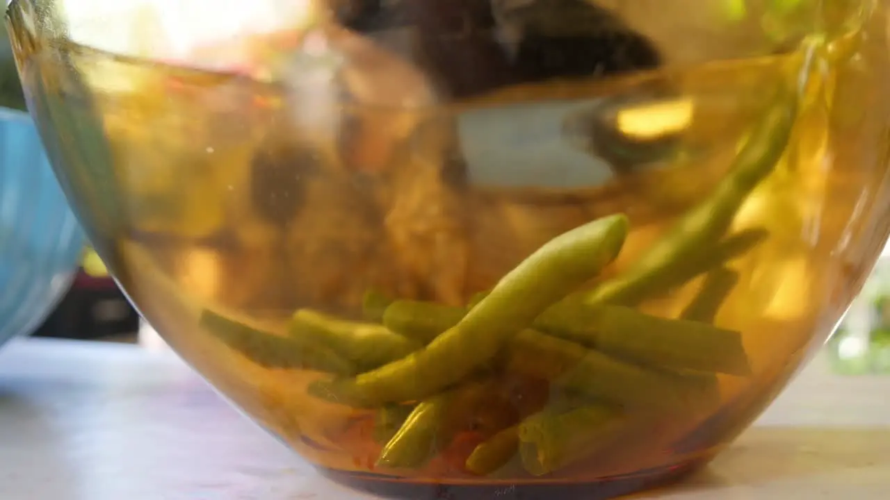 Close Up Of Glass Bowl With Vegetables While Elder Woman Cuts Vegetables In Background In Slow Motion