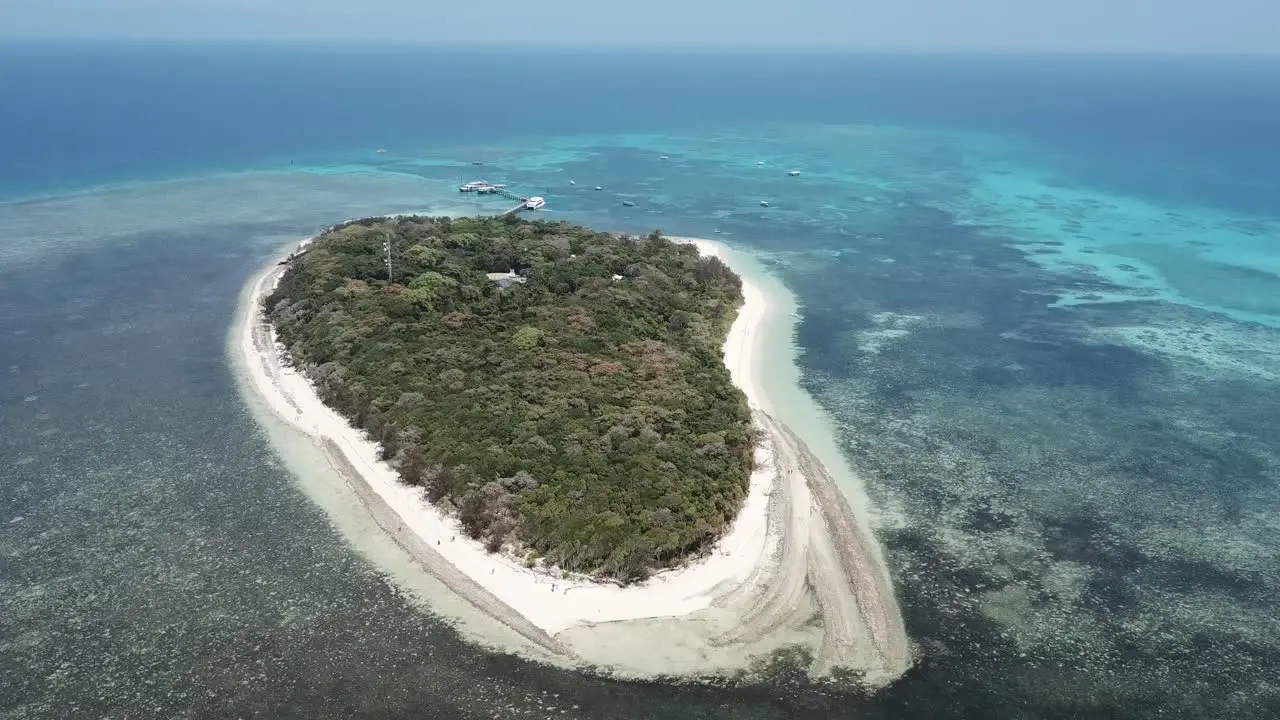 Drone aerial pan around a small tropical island with trees and blue clear water