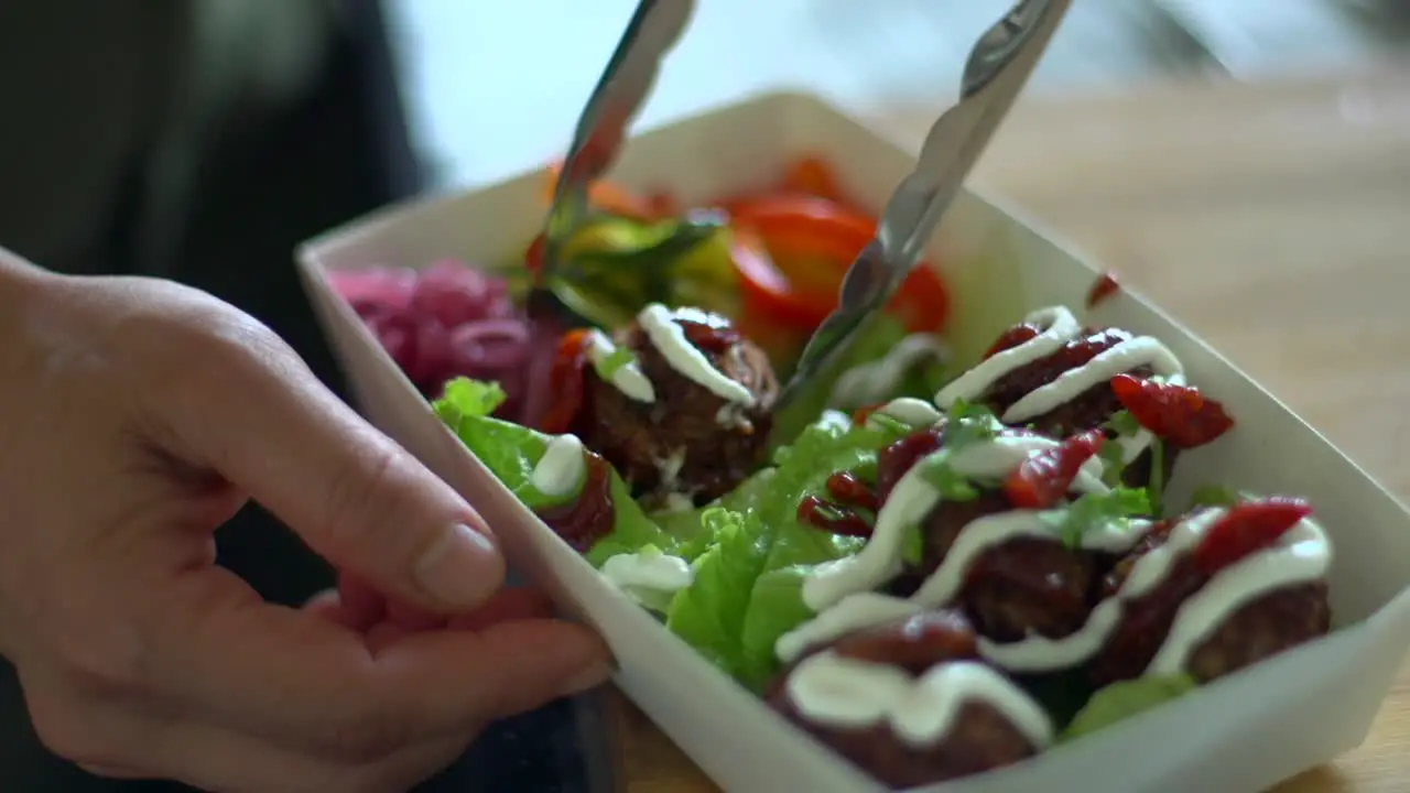 Meat balls being rotated and positioned in container of salad filmed as close up shot in handheld slow motion style