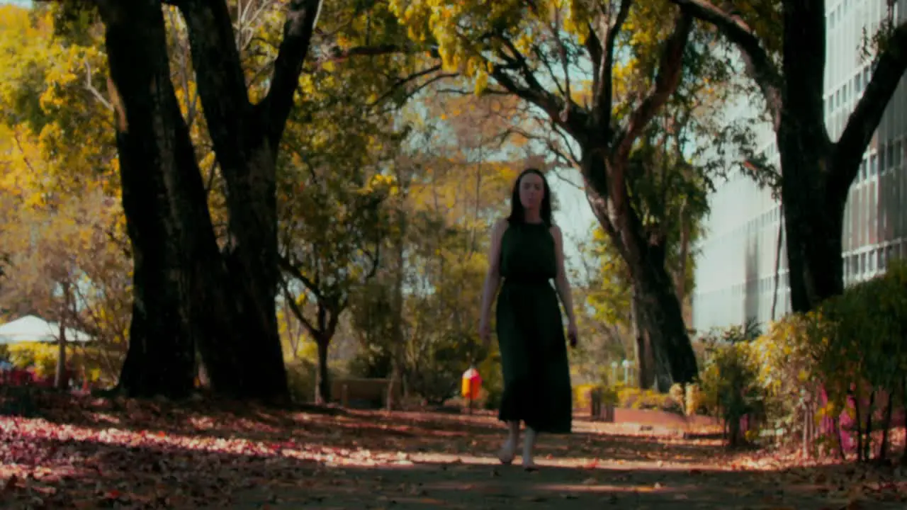 Handheld shot of confident woman in green dress walking in park towards camera