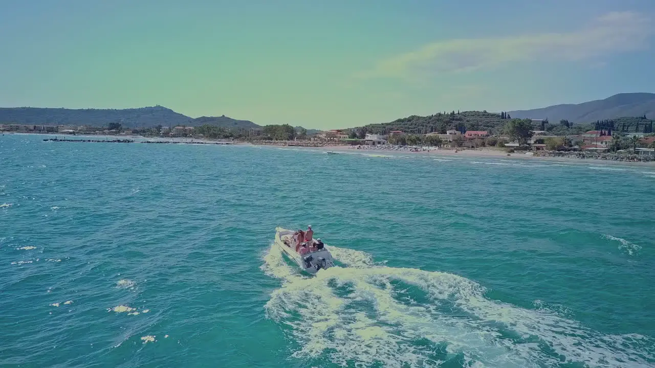 Aerial following boat along shoreline in bright blue ocean water on sunny day