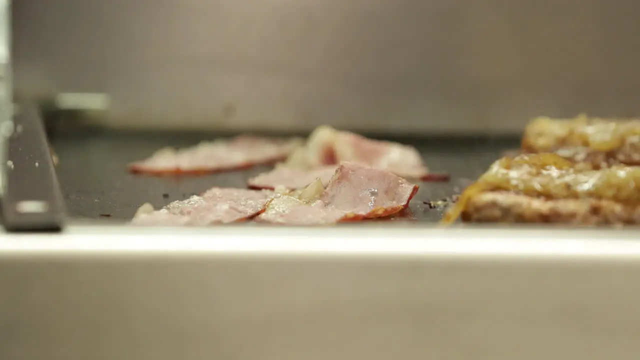 Cooking Bacon And Burger Patties On A Stainless Griddle Adding Slice Of Cheese On Top Of A Patty close up