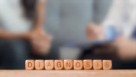 Medical Concept With Wooden Letter Cubes Or Dice Spelling Diagnosis Against Background Of Doctor Talking To Patient