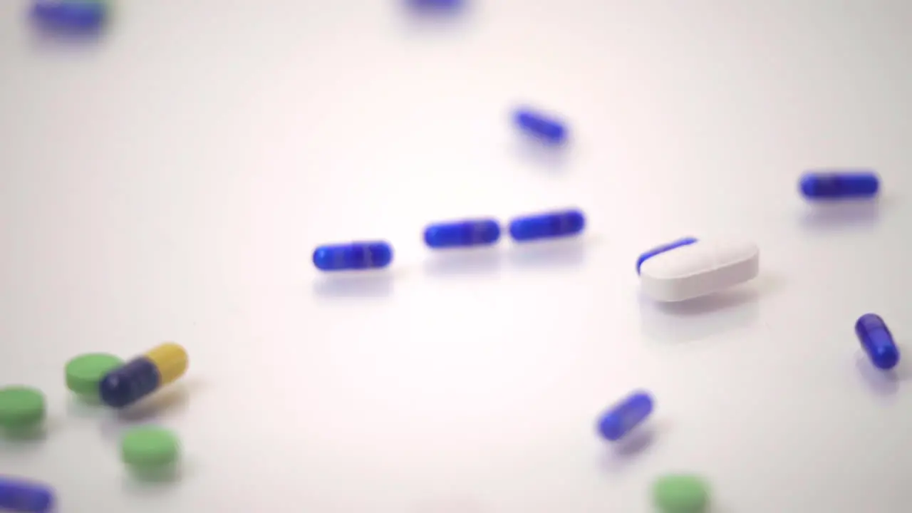 Macro of Pill Varieties Sliding onto One Blue and Yellow Pill on White Background