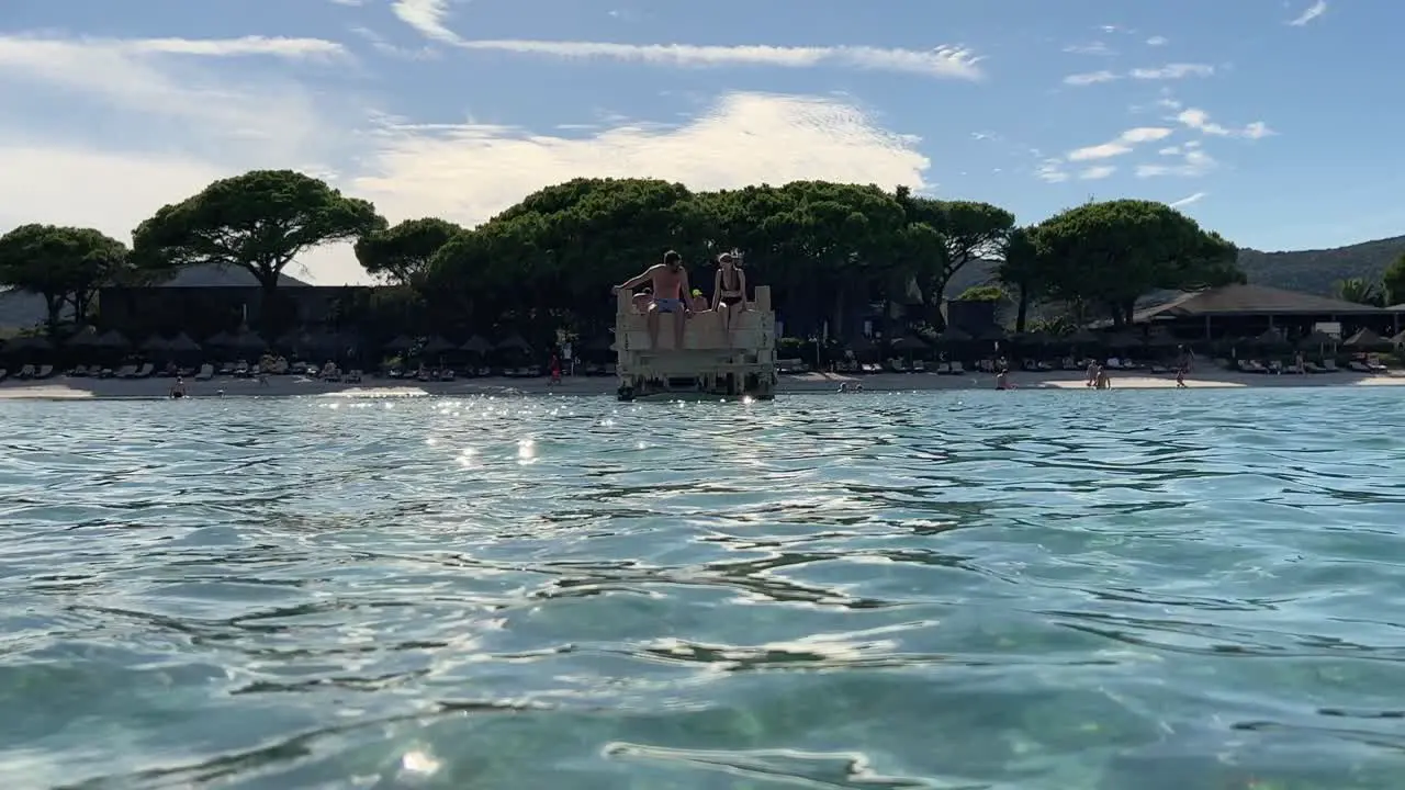 People sitting on edge of wooden pier of Santa Giulia beach in Corsica island France