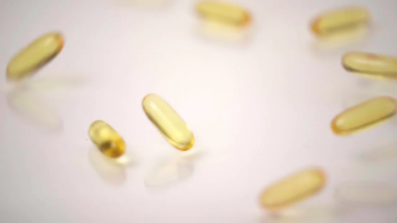 Slow Motion Macro of Yellow Pills Dropped onto White Background