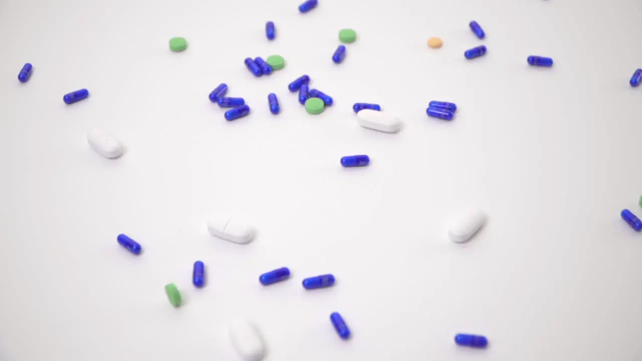 Pill Varieties Dropped onto White Background as Hand Reaches in to Pick Up Casing