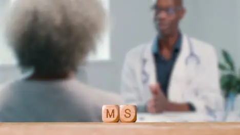 Medical Concept With Wooden Letter Cubes Or Dice Spelling MS Against Background Of Doctor Talking To Patient