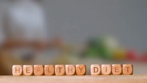 Medical Concept With Wooden Letter Cubes Or Dice Spelling Healthy Diet Against Background Of Woman Chopping Ingredients