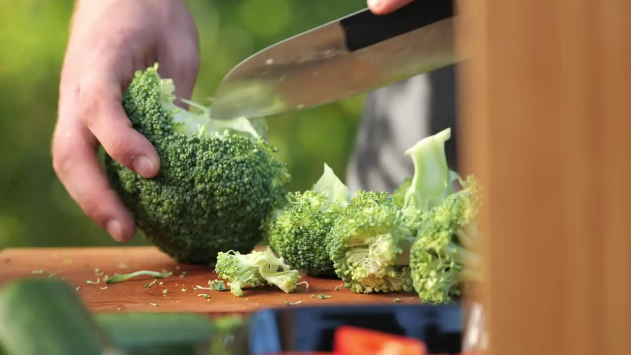 A young man chops a broccoli on a wooden board close up