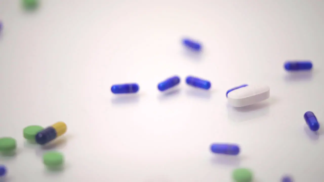 Slow Motion Macro of Pill Varieties Sliding onto One Blue and Yellow Pill on White Background