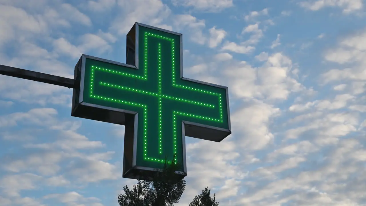 Illuminated green pharmacy cross in front of the drugstore