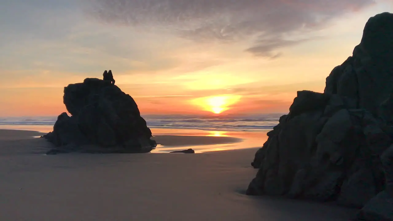 Two people sitting on a tall rock at Devil's Kitchen which is a part of Bandon Beach State Park at the Oregon Coast enjoying a peaceful and beautiful sunset