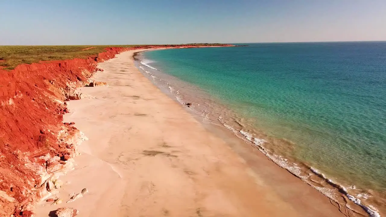 Aerial footage of male and female couple sitting atop red cliff overlooking beach and blue ocean